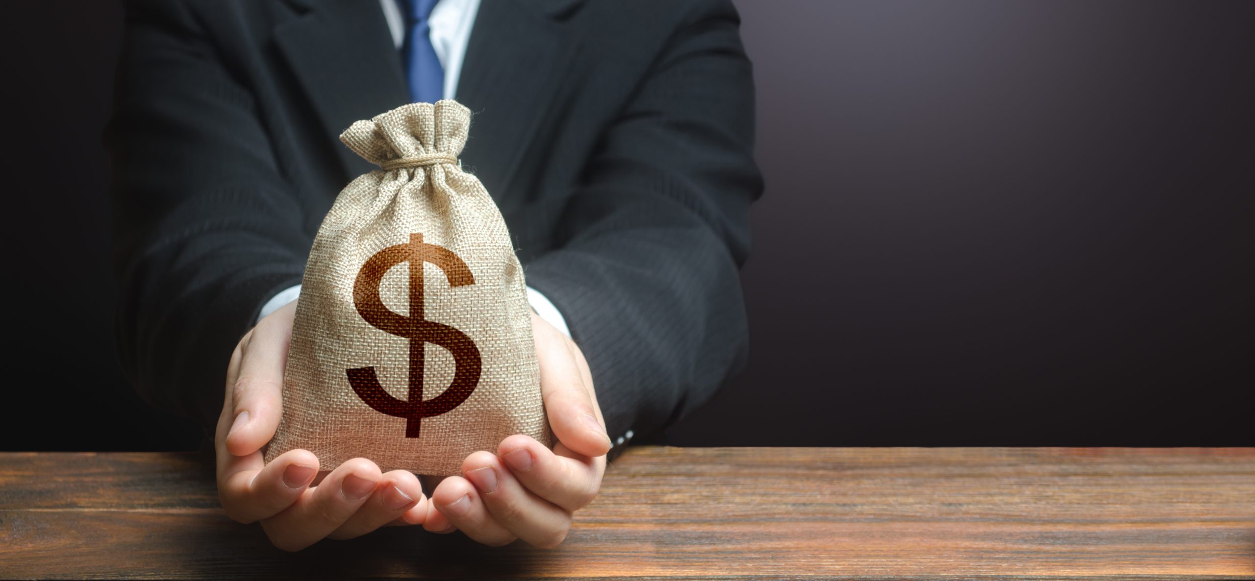 Businessman holds out dollar money bag.